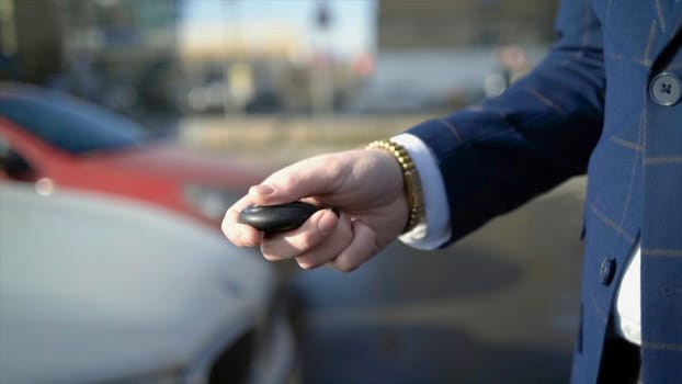 Close-up of businessman pressing car key. Action. Businessman opens car with electronic key and looks at phone. Modern car key to open and start it.