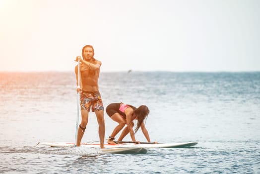 Sea woman and man on sup. Silhouette of happy young woman and man, surfing on SUP board, confident paddling through water surface. Idyllic sunset. Active lifestyle at sea or river