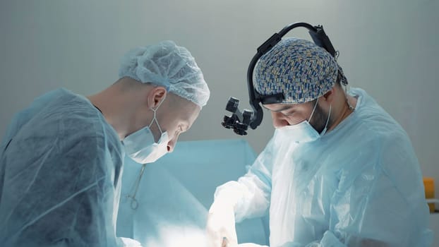 Two surgeons busy at work . Action . Two men in blue lab coats are painstakingly working on a complex operation , using various medical accessories like microscopic glasses . High quality 4k footage