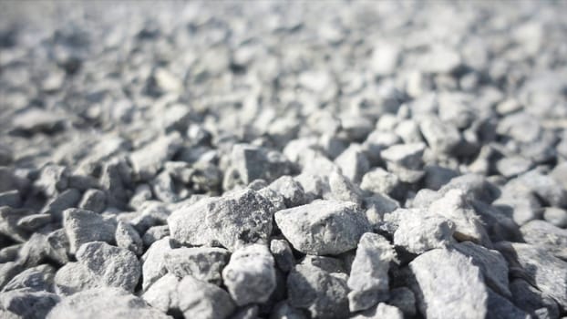 Background of gray granite gravel under the bright sun. Close up of white stones falling down on the ground, pebble texture.