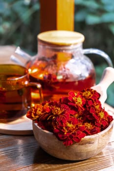 Marigold tea still life on table in green garden background. Healthy hot drink benefits. Natural organic aromatic drink in cup. Home-grown immunity-boosting herbs for tea. Autumn winter warming calming drink