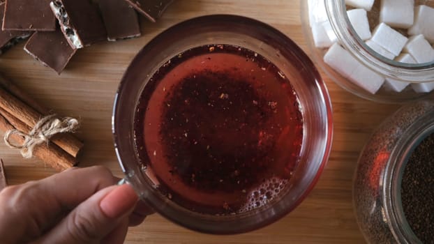 Process of brewing red karkade tea, close up top view. Cup of freshly brewed fruit tea, pouring hot water from the kettle into a glass cup on wooden background.