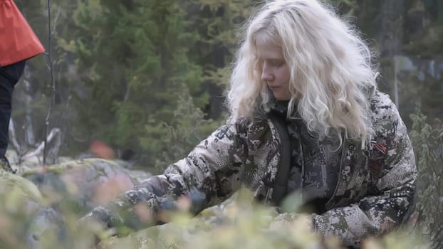 MOSCOW, RUSSIA - FEBRUARY 25, 2022 : A girl with blonde hair eats berries sitting in the grass. CLIP. During the hiking trip, the travelers stopped to eat wild berries.