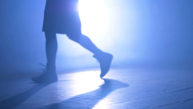 Bottom view of fighter training in the gym with smoke and light background. Muscular man in smoke on dark background. Close up of athlete or sportsman moving fast while training with smoke and light on background. Silhouette of strong male boxer on dark background