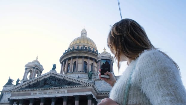 Beautiful young woman takes photos of Cathedral on phone. Concept. Attractive woman takes pictures of domed Cathedral which is popular attraction in old city.