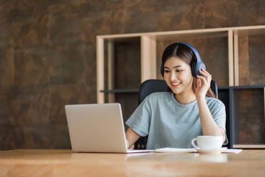 Young female student wearing headphones sits intently and happily studying online on her laptop in the living room at home..