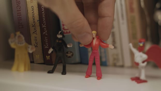 Close up of retro toys of Bremen Musicians standing on a wooden bookshelf with books on the background. Hand puttin small toy figure of Troubadour.