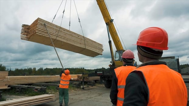 Worker in a construction site transporting a wooden bars using crane. Workers are used wooden ladder at construction site. Reinforced steel bars are protruding from the concrete pillar, base for new edifice. Transporting. Bonding of wooden bars.