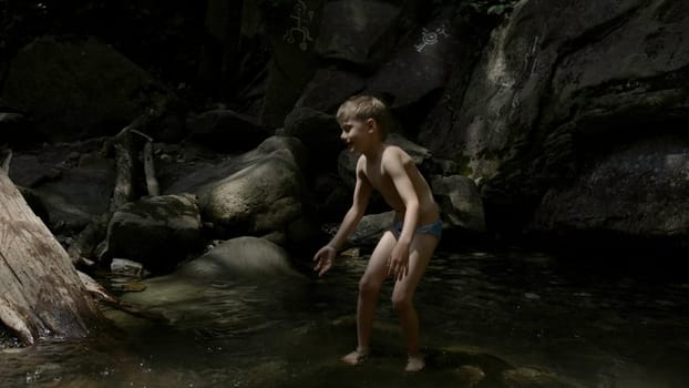 A child on a journey. Creative. A little boy in underpants playing in the water and large rocks from the cliff are visible from behind. High quality 4k footage