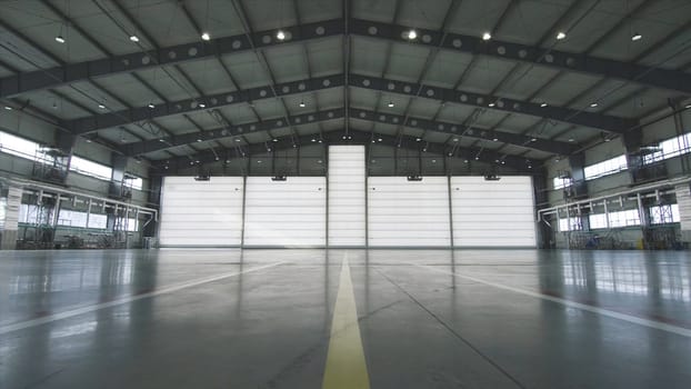 Roller shutter door and concrete floor inside factory building for industrial background. Airplane in front of half opened door to hangar. The open door of the hangar. Mechanic opening the door of a airplane hangar