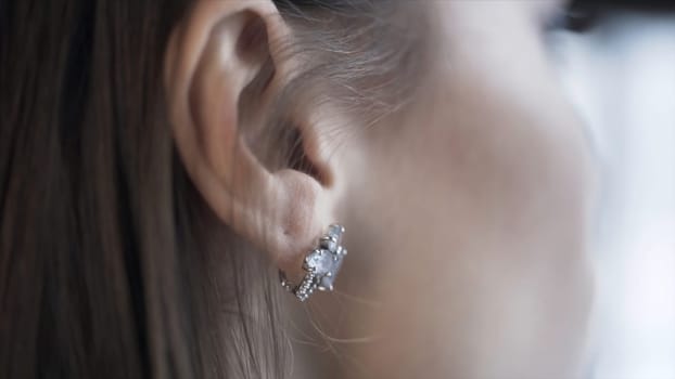 Close up of brunette woman hand pushing her hair back behind her ear and baring a silver earring. Side view of a girl face touching her dark hair.