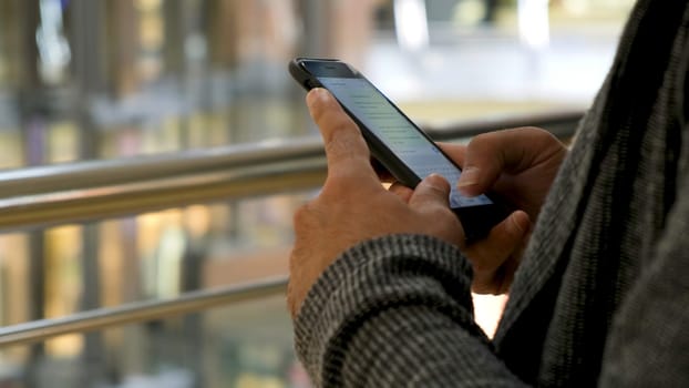 Close up of man hands texting a message on shopping mall background. Male hands using his smartphone for chatting in social net.