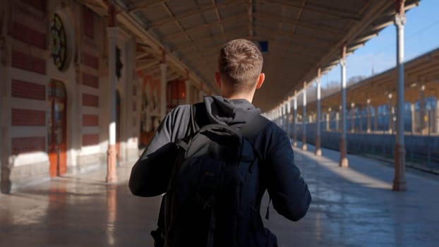 Young man with backpack walking along empty railway station. Action. Travel concept