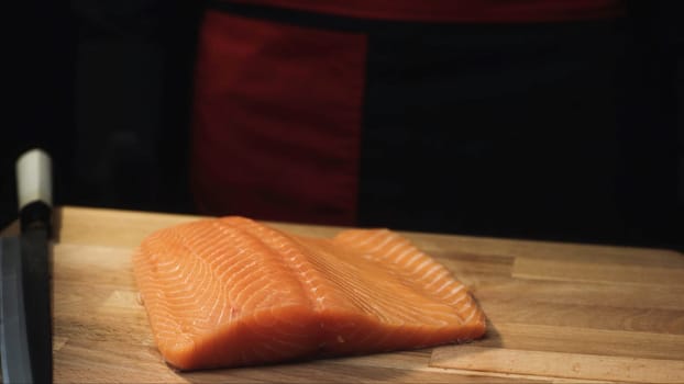 Close-up of raw salmon fillet on wooden board with knife. View of juicy piece of salmon before cutting to prepare delicious dish.