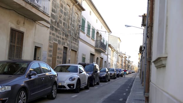 View of narrow streets of european city in summer. Art. Woman walks with dog on narrow street with parked row of cars on summer vacation.