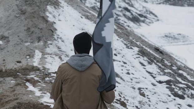 Amazing view on man who climbing with a flag on the top of the mountain, rear view. Footage. Businessman hand wanting for victory white flag on mountain peak with sky cityscape background.
