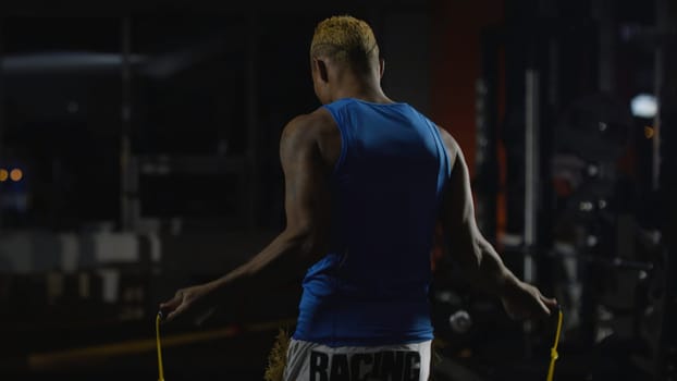 Full length portrait of a boxer jumping with skipping rope. Athletic, muscular young boxer shirtless with jumping rope ready to jump. Middle aged boxer warming up with jumping rope in a fight club, rear view 4K