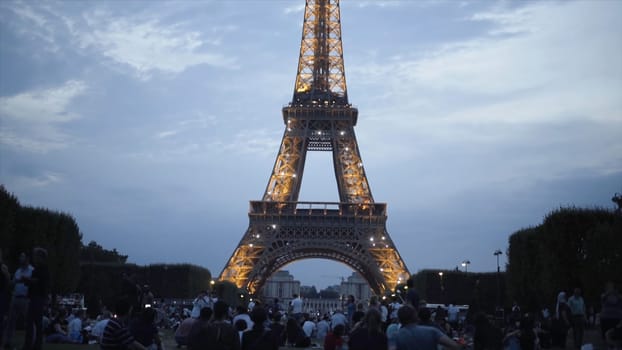 Tourists at shining Eiffel tower in evening. Action. Many tourists sit on lawn and enjoy beautiful view of shining Eiffel tower in evening in summer.