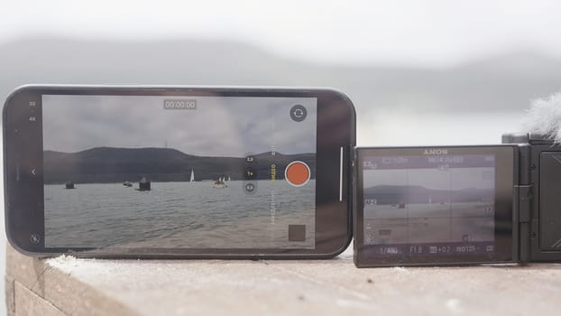 Turkey, Istanbul - August 10, 2022: Comparing videos on phone and camera. Action. Close-up phone screens and cameras capture landscape. Comparison of video recording on phone and camera.