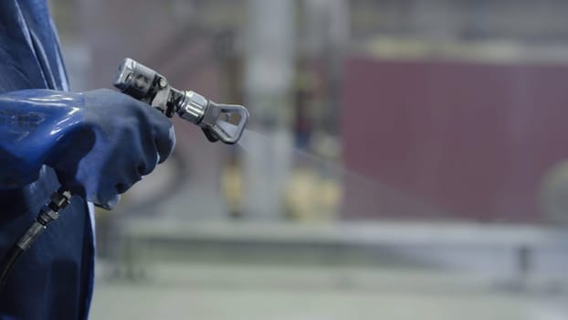 Arm hand holding industrial size spray gun used for industrial painting and coating. Male hand holding paint spray, closeup.
