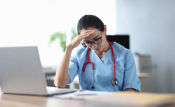 Tired doctor sitting at table and holding his head. Medical error concept