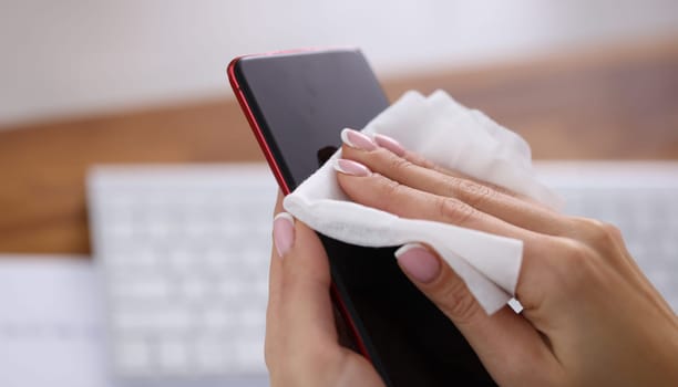 Woman wiping screen of mobile phone with damp cloth closeup. Antiseptic during covid19 pandemic concept