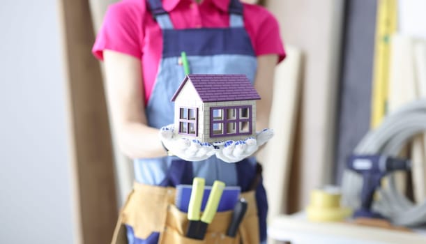 Woman builder holding toy wooden house in hands closeup. Construction and repair of houses concept
