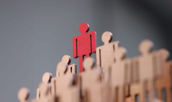 Red wooden figurine standing above others closeup. Leadership skills concept