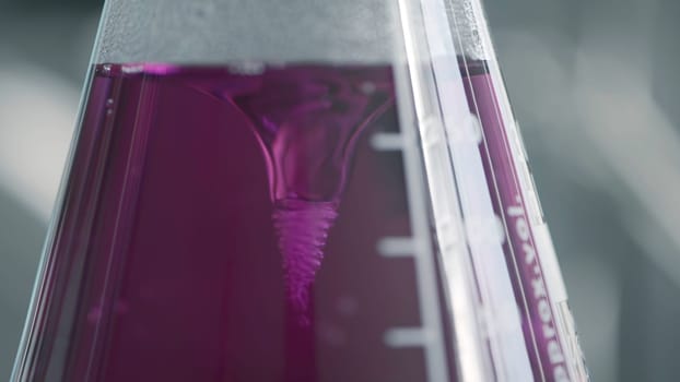 View inside of a laboratory, making tests with a pink liquid inside flask. Action. Concept of research, biochemistry, pharmaceutical medicine