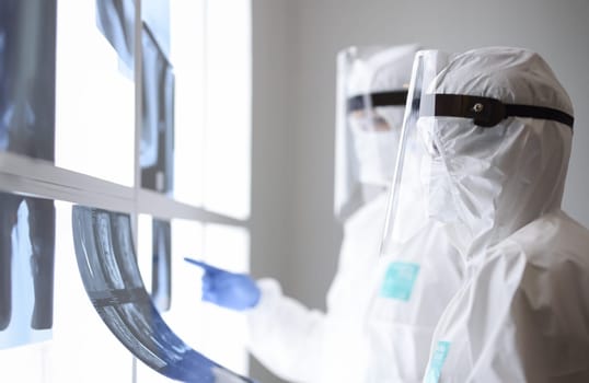 Doctors in protective suits are looking at x ray in clinic. Diagnosis of covid pneumonia concept