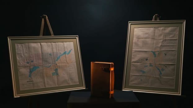 Exposition of old leather bound notebook between two old maps standing in te dark room. Museum exhibition