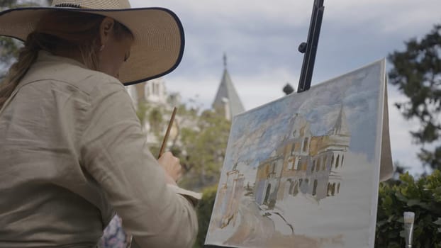 Woman paints in nature. Action. Woman in vintage style paints an oil painting on canvas. Beautiful woman in old outfit paints picture of nature on sunny day.