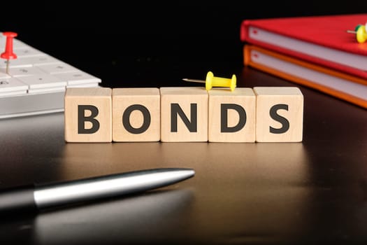 BONDS the text of non-wooden cubes next to notepads, a calculator, a pen on a black background