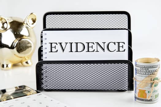 EVIDENCE text on a white piece of paper next to a piggy bank, a roll of money and a calculator on a white background