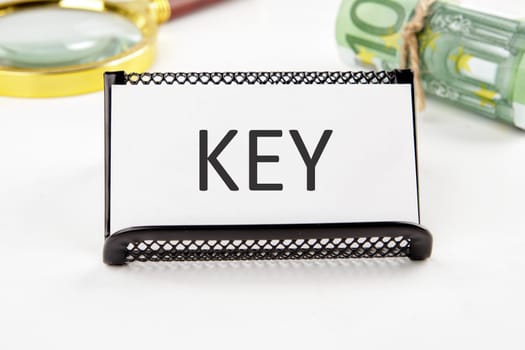 KEY the text on the business card next to the roll of money with a magnifying glass in the background is out of focus on a white background