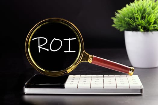 Return on investment concept. ROI text seen with a magnifying glass on a black background