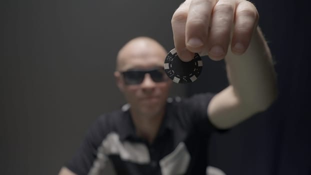 Man drops chip on poker table. Action. Bandit with glasses drops chip on pile of chips on poker table. Gambling and crime.