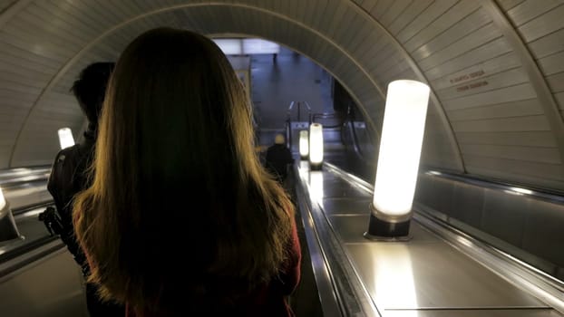 Rear view of girl girl down the escalator in the subway. Woman coming down to the metro station through the escalator tounel. woman riding up an escalator in a metro station 4K