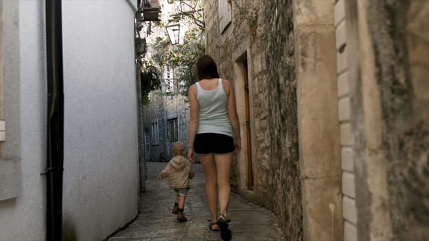 Woman with child walking around European city. Creative. Woman and son are walking around ancient city. European city with ancient stone architecture and walking tourists.