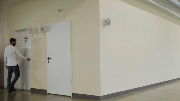 Young man walking inside the public bathroom inside shopping mall. HDR. Man entering toilet room