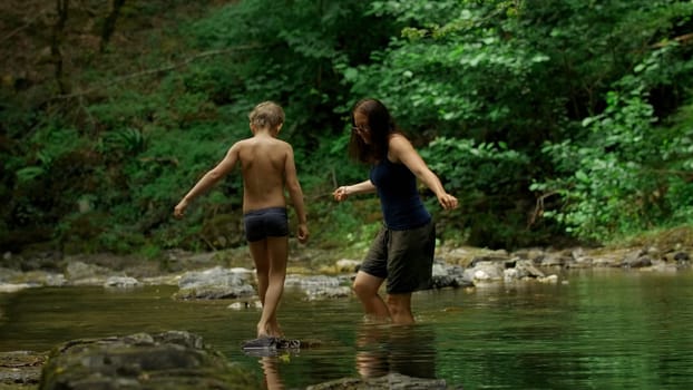 Mother and her boy child in forest stream. Creative. Hiking in wild jungles on a summer day