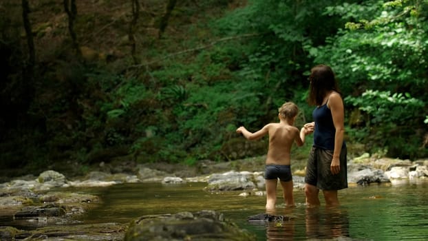 Mother and her boy child in forest stream. Creative. Hiking in wild jungles on a summer day