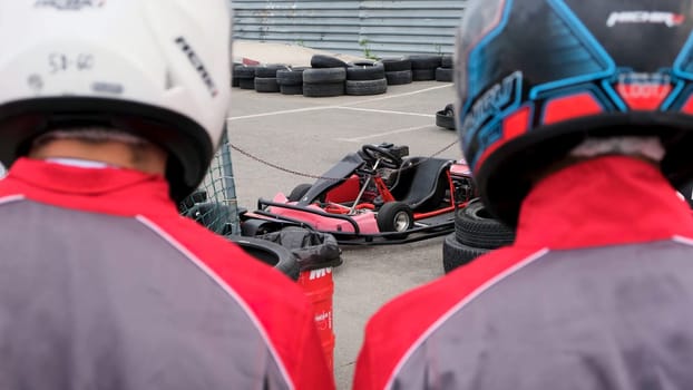 Close up of racer backs wearing special uniforms and helmets going to the kart cars, competition and race concept. Rear view of two men before the karting race.