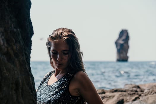 Woman travel sea. Young Happy woman in a long red dress posing on a beach near the sea on background of volcanic rocks, like in Iceland, sharing travel adventure journey