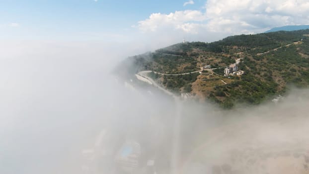 Top view of mountain resort through clouds. Shot. Beautiful view of mountain coast town in clouds. Thick clouds with view of city in mountains in summer.