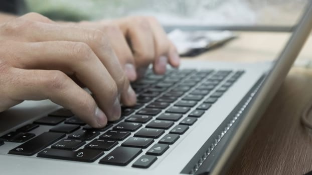Close-up of man typing on laptop keyboard. Stock footage. Freelancer or businessman works on laptop. Men's hands print text or article on laptop.