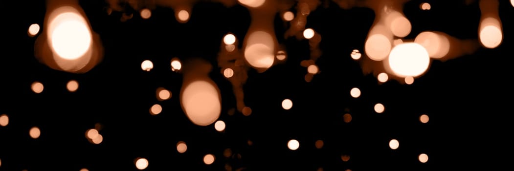 Blurry garland lights on a dark background. Festive Christmas and New Year background. Soft focus. Image toned in color of the year 2024 - Peach Fuzz.