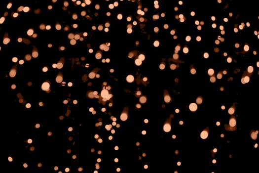 Blurry garland lights on a dark background. Festive Christmas and New Year background. Soft focus. Image toned in color of the year 2024 - Peach Fuzz.