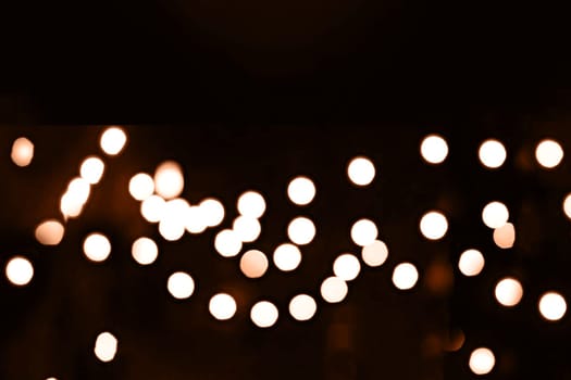 Blurry garland lights on a dark background. Festive Christmas and New Year background. Soft focus. Image toned in color of the year 2024 - Peach Fuzz.