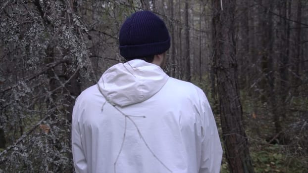Close-up portrait of young man from back against thick dark forest in autumn. Footage. Concept of research journeys.